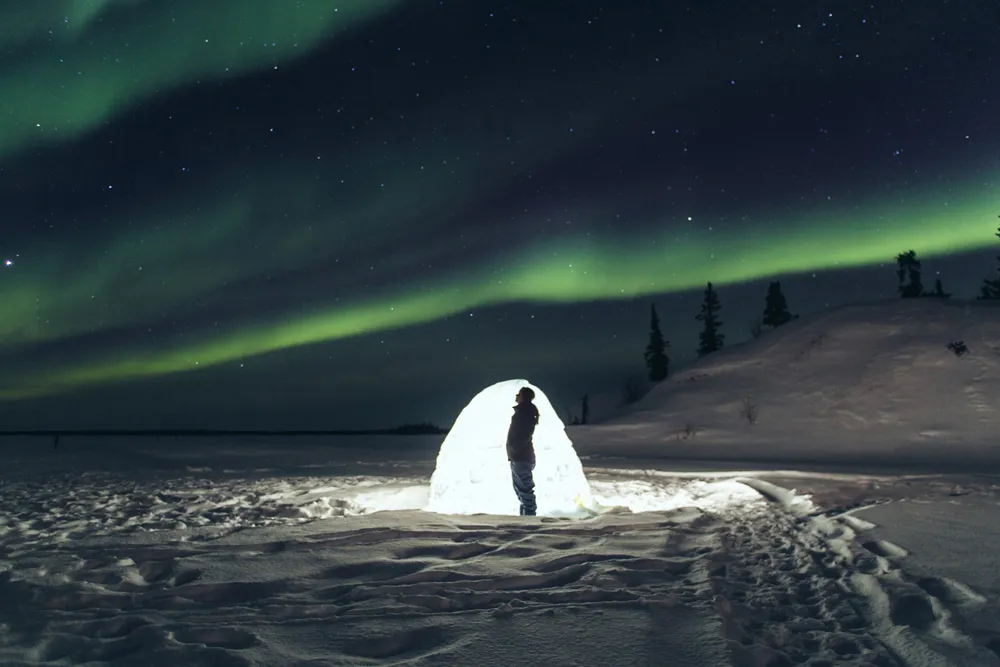 Voyageur devant un igloo sous un ciel couvert d’aurores boréales, Territoires du Nord-Ouest, Canada | © iStock / unaz