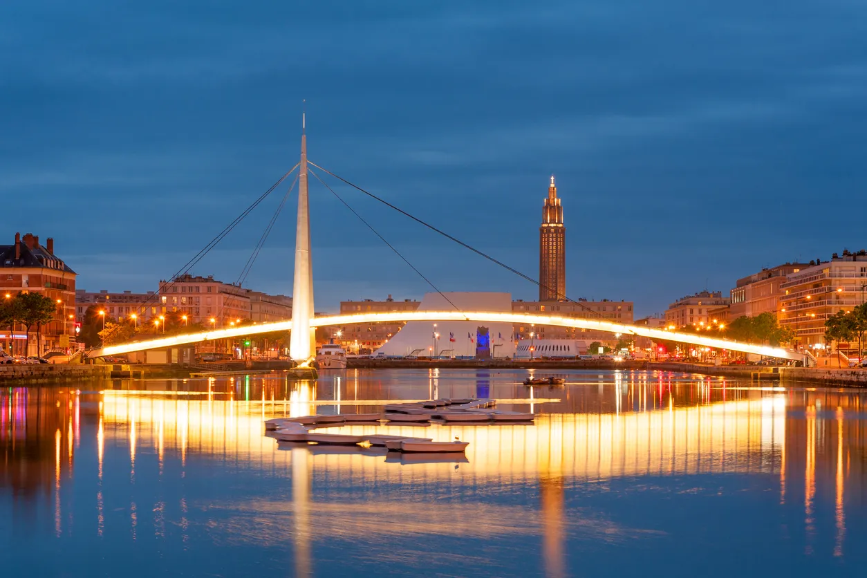 La passerelle François Le Chevallier, de l'architecte de Guillaume Gillet, enjambe le bassin du Commerce. Derrière, la Maison de la Culture du Havre, conçue par l'architecte brésilien Oscar Niemeyer et surnommée "le volcan".  © iStock / Tashka