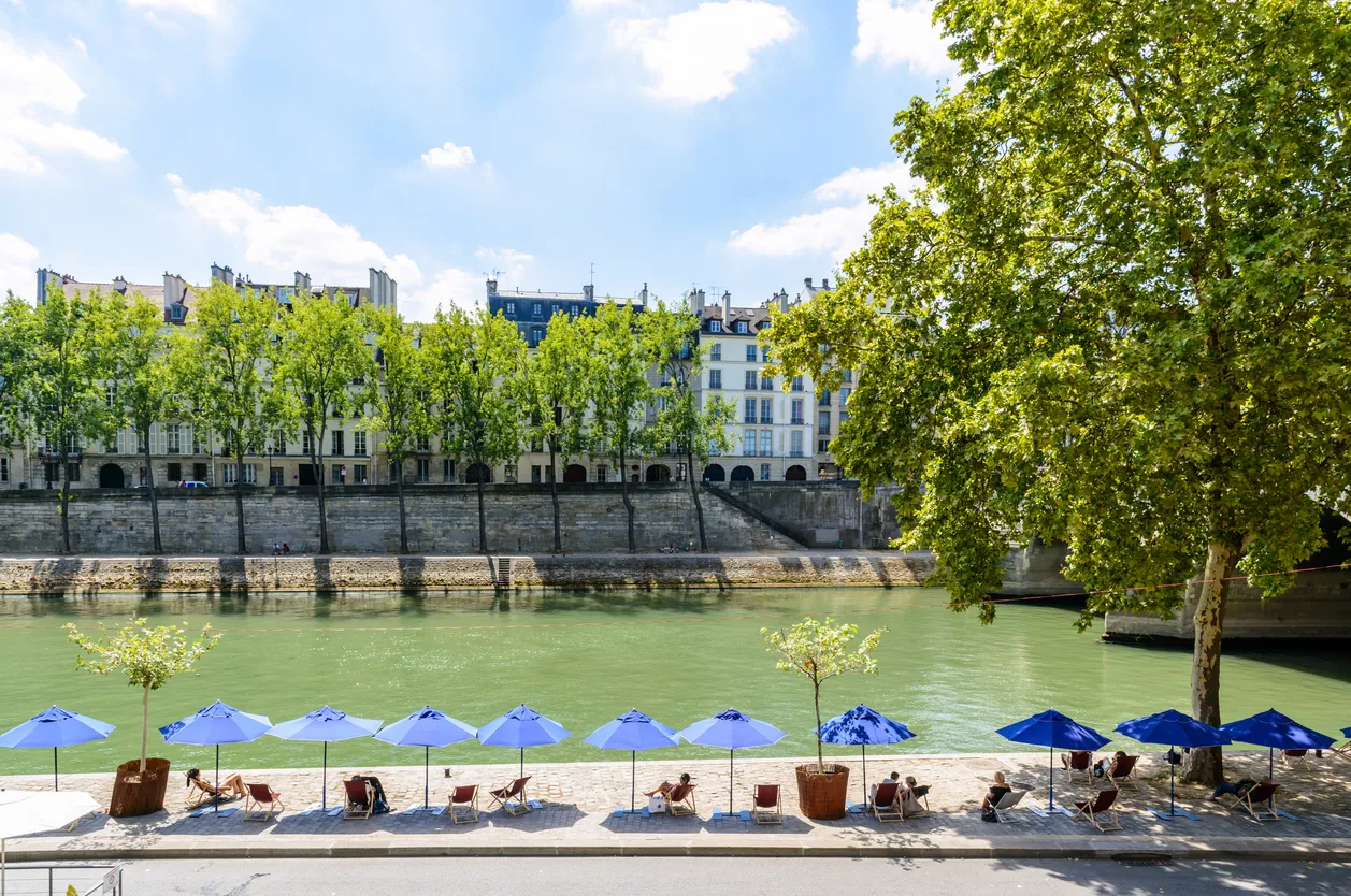 Les rives de la Seine avec chaises longues et parasols pendant Paris-Plages avec les bâtiments de l’Ile de la cité en arrière-plan. © iStock / olrat