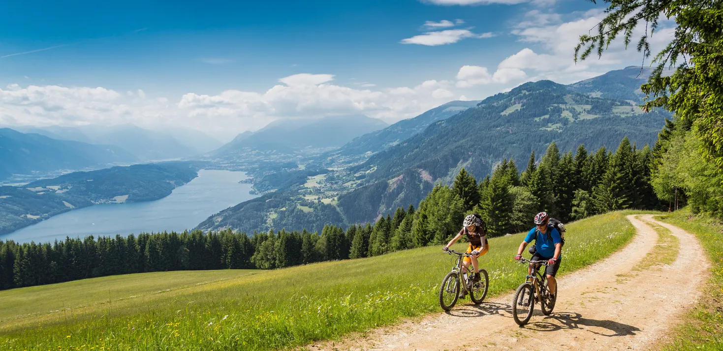 Deux cyclistes en montée sur une route forestière pittoresque en Carinthie, dans le sud de l'Autriche, avec le lac Millstätter en arrière-plan. © iStock / Saro17
